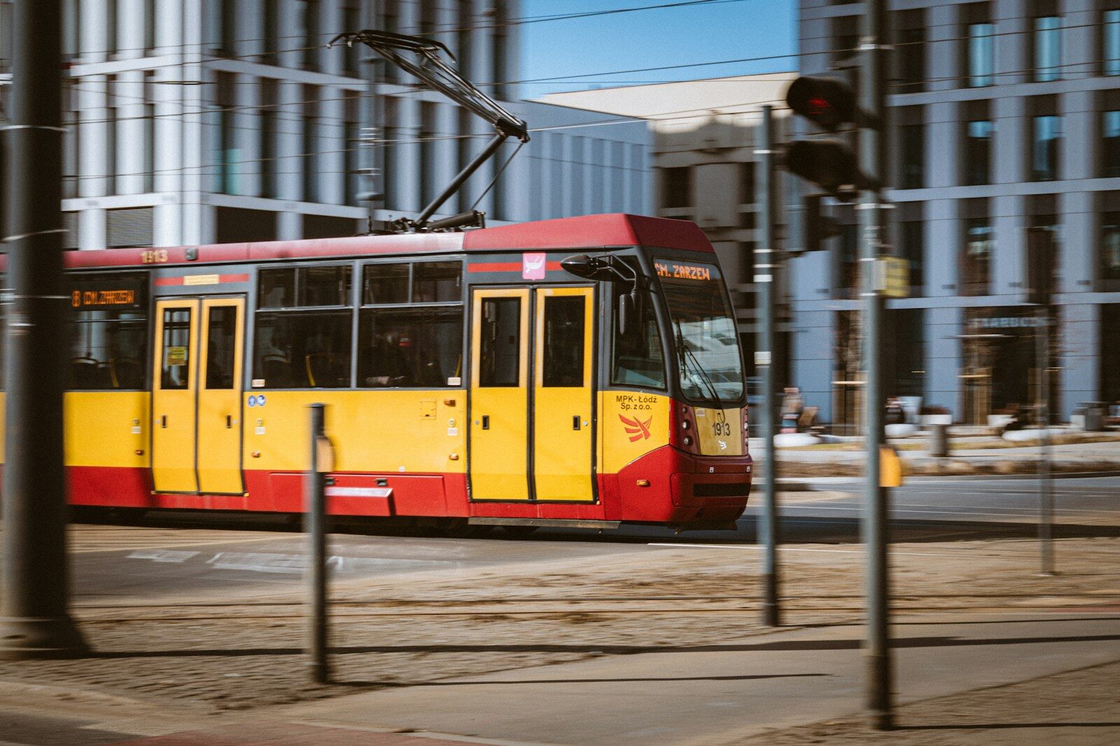 A yellow and red tram moves through a city street.